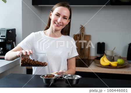 Woman pours dog food for pets into a steel bowl in the kitchen Woman pours dog food for pets into a steel bowl in the kitchen 100446001
