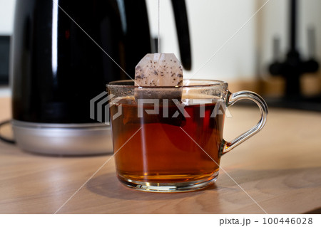 A teapot pouring boiling water into a cup. A bag of black tea is put in a mug 100446028