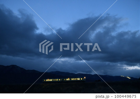 北杜市小淵沢町、スキー場の照明が灯る夕暮れの小海線築堤を行く下り列車 100449675