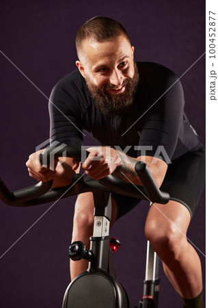 Man smiling on exercise bike dark background, man doing cardio workout on exercise bike, fat burning, weight loss, sport lifestyle concept 100452877