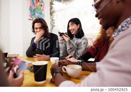 A company of young people in a cafe, have fun, drink coffee, have fun browsing social networks with a cheerful company, modern young people with laptops and smartphones A company of young people in a cafe, have fun, drink coffee, have fun browsing social networks with a cheerful company, modern young people with laptops and smartphones 100452925