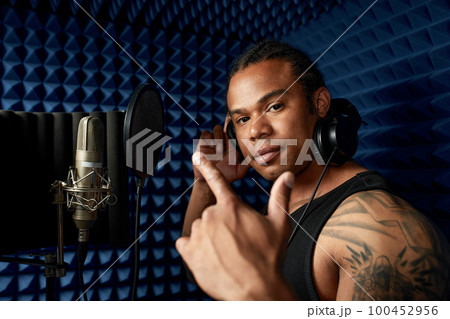 Close-up of an afro american rap artist with headphones while recording a song at a recording studio 100452956