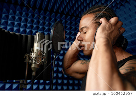 Close-up of an afro american rap artist with headphones while recording a song at a recording studio Close-up of an afro american rap artist with headphones while recording a song at a recording studio 100452957