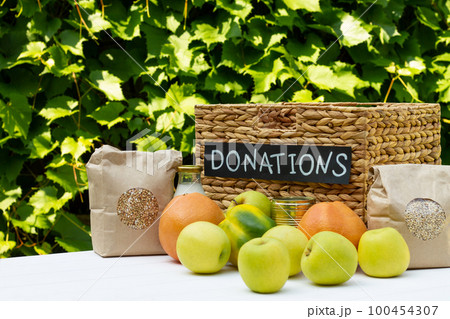 Various food in a box for donations on a table on a background of greens. Charity and donation concept, copy space. Various food in a box for donations on a table on a background of greens. Charity and donation concept, copy space. 100454307