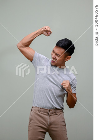Happy Asian man raising hand up, rejoicing, dancing with joy, yes gesture 100460576