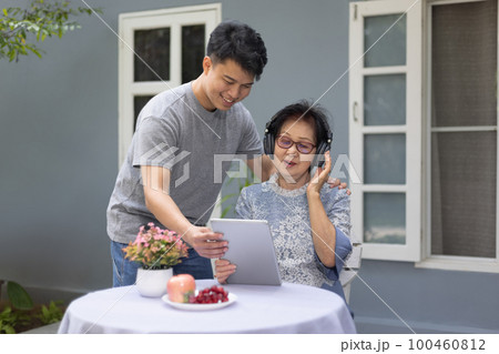 Grandson helping grandmother using computer tablet for listen music and pose share good news at social media. Grandson helping grandmother using computer tablet for listen music and pose share good news at social media. 100460812