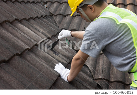 Worker man using waterproof roof coating repair to fix crack of the old tile roof. Worker man using waterproof roof coating repair to fix crack of the old tile roof. 100460813