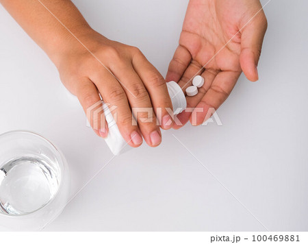 Close-up of woman pouring pills from bottle for medicinal purposes. Woman holding pills in hand with water. Healthcare, medicine, treatment, therapy concept 100469881