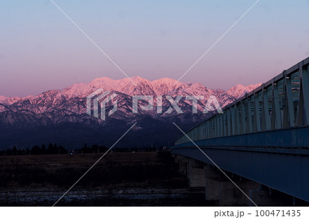 夕陽に染まる常願寺川に架る大日橋と北アルプス毛勝山雪景色 100471435