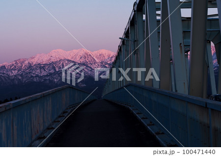 夕陽に染まる常願寺川に架る大日橋と北アルプス毛勝山雪景色 100471440