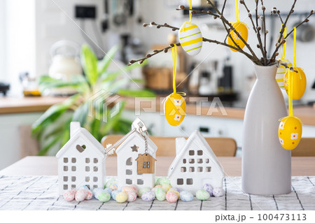 Key to house of cozy home with Easter decor with rabbit and eggs on table of kitchen. Building, design, project, moving to new house, mortgage, insurance, rent and purchase real estate 100473113