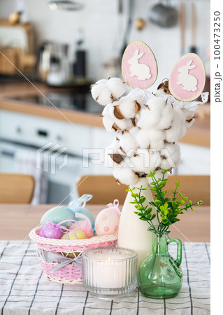 Easter decoration of colorful eggs in a basket and a rabbit on the kitchen table in a rustic style. Festive interior of a country house Easter decoration of colorful eggs in a basket and a rabbit on the kitchen table in a rustic style. Festive interior of a country house 100473250