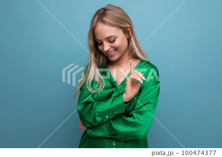 young cute woman in a green shirt shyly looks at the floor on a blue studio background young cute woman in a green shirt shyly looks at the floor on a blue studio background 100474377