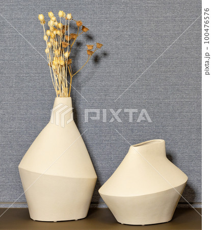 Figured clay vases with dry flower stems on a gray fabric wall background. 100476576