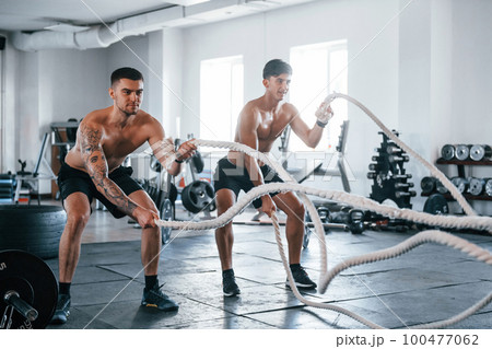 Young people with sportive body shapes doing crossfit by using knots Young people with sportive body shapes doing crossfit by using knots 100477062