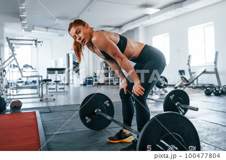 Young fitness woman with slim type of body doing exercises by using barbell Young fitness woman with slim type of body doing exercises by using barbell 100477804