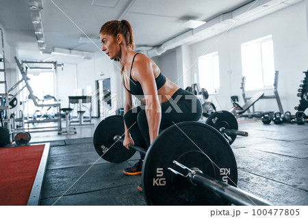 Young fitness woman with slim type of body doing exercises by using barbell 100477805