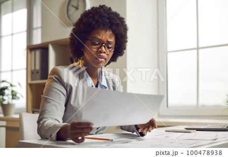 Serious focused businesswoman sitting at desk looking at paper document 100478938