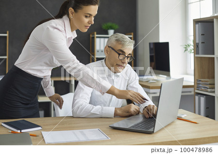 Young woman director views the project of the employee on the laptop screen, shows the inaccuracies of the project. 100478986