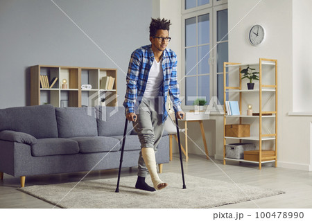 Handicapped young african man with broken leg trying to walk with crutches. 100478990