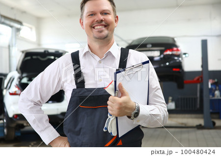 Portrait of caucasian auto mechanic with clipboard of maintenance documents and checking car damage in auto garage 100480424