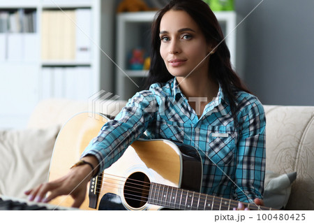 Talented young woman holding guitar in hands at home 100480425