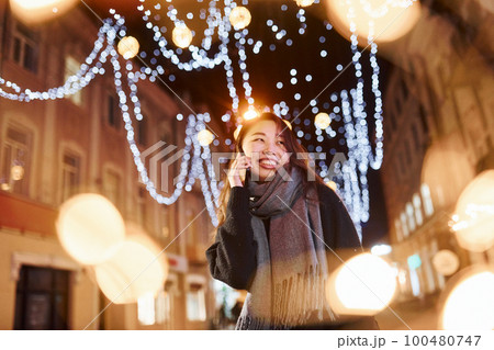 Talks by phone. Cute and happy asian young woman outdoors in the city celebrates New year 100480747
