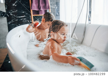 Two kids having fun and washing themselves in the bath at home. Helping each other Two kids having fun and washing themselves in the bath at home. Helping each other 100482299