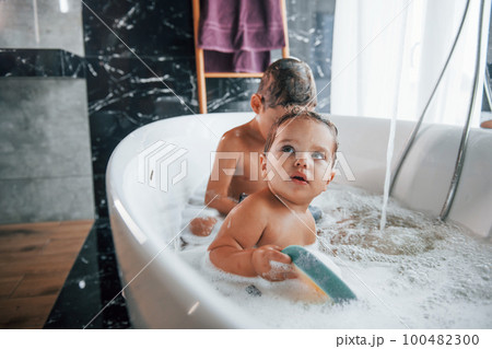 Two kids having fun and washing themselves in the bath at home. Helping each other Two kids having fun and washing themselves in the bath at home. Helping each other 100482300