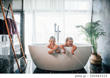 Two kids having fun and washing themselves in the bath at home. Posing for a camera Two kids having fun and washing themselves in the bath at home. Posing for a camera 100483524