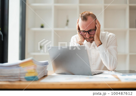 Tired businessman looking at laptop while sitting at desk in office 100487612