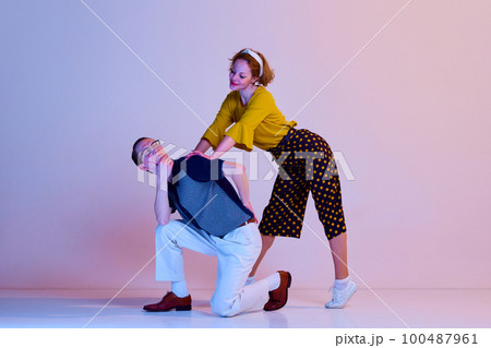 Emotional young couple, man and woman in stylish clothes dancing retro dance against gradient pink purple studio background 100487961
