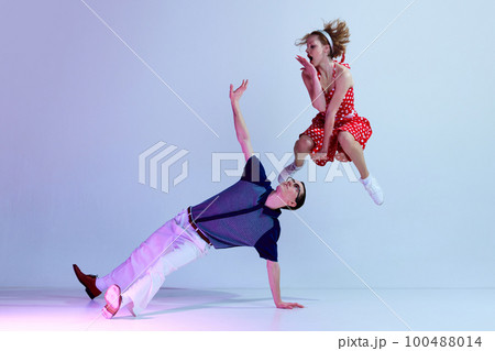 Jumping. Beautiful girl and man in colorful costumes dancing retro style dances against gradient blue purple studio background 100488014