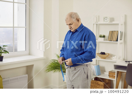 Senior man measuring waist with tape at home Senior man measuring waist with tape at home 100491220