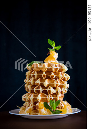Cooked sweet Belgian waffles with oranges on a black 100493125
