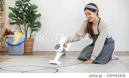 Housekeeper is using cordless vacuum cleaner with handheld for cleanups and vacuuming dirt on carpet 100493826