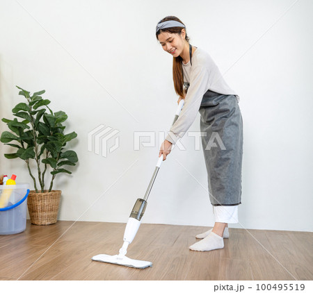 Housekeeper is use mop with vacuum cleaner to housekeeping with vacuuming and wiping dirty laminate on the floor in living room while working to perform routine house cleaning Housekeeper is use mop with vacuum cleaner to housekeeping with vacuuming and wiping dirty laminate on the floor in living room while working to perform routine house cleaning 100495519