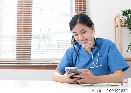 Veterinarian woman in blue uniform is using smartphone to searching pet information and writing data 100495835