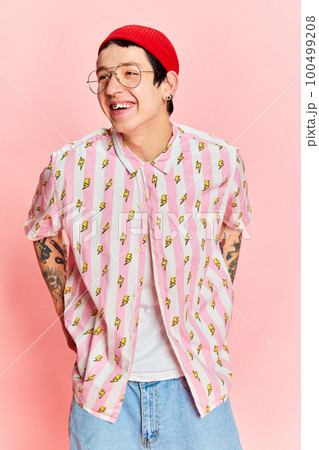 Portrait of fashionable modern stylish guy wearing glasses keeping hands in pockets and looking away isolated on pink background. 100499208