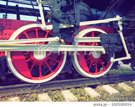Retro vintage wheels of a locomotive or train close up. Red large heavy metal wheels with piston guiding mechanisms. Locomotive of the 19th - 20th centuries with a steam engine. Retro style Retro vintage wheels of a locomotive or train close up. Red large heavy metal wheels with piston guiding mechanisms. Locomotive of the 19th - 20th centuries with a steam engine. Retro style 100500954