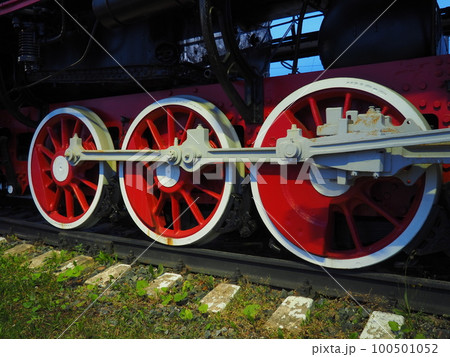 Retro vintage wheels of a locomotive or train close up. Red large heavy metal wheels with piston guiding mechanisms. Locomotive of the 19th - 20th centuries with a steam engine. Bright vivid photo 100501052