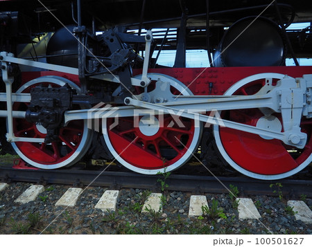 Retro vintage wheels of a locomotive or train close up. Red large heavy metal wheels with piston guiding mechanisms. Locomotive of the 19th - 20th centuries with a steam engine. 100501627