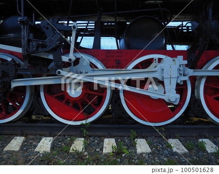 Retro vintage wheels of a locomotive or train close up. Red large heavy metal wheels with piston guiding mechanisms. Locomotive of the 19th - 20th centuries with a steam engine. 100501628