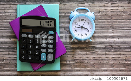 Colored notepads, alarm clock and calculator with display text LIMIT on wooden table 100502671