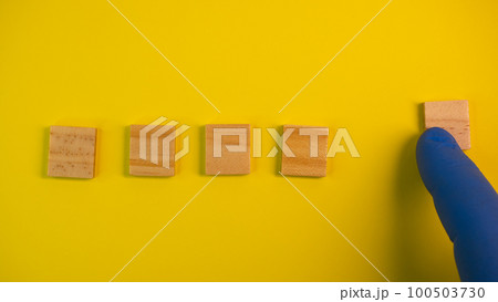 Hand in blue gloves point on clean wooden blocks on colored yellow background. Medical scientific or biological theme. Template for text or concept. Advertising mock up. Presentation flat lay mock up 100503730