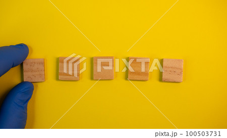 Hand in blue gloves point on clean wooden blocks on colored yellow background. Medical scientific or biological theme. Template for text or concept. Advertising mock up. Presentation flat lay mock up 100503731