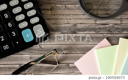 On a wooden background magnifier, calculator, notepad 100504073