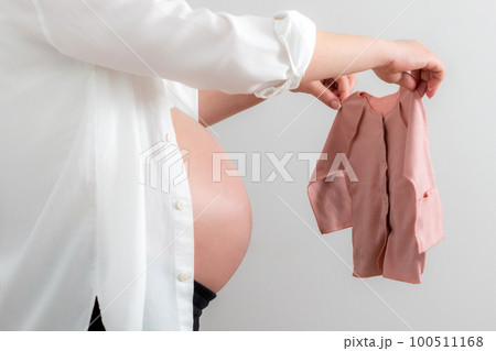 Pregnant woman holding baby clothes as a concept of expecting a baby Pregnant woman holding baby clothes as a concept of expecting a baby 100511168