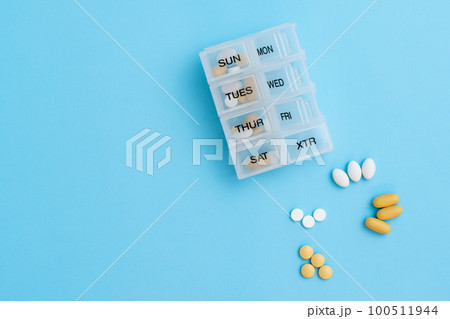 Top view of pill organizer with variety of pills and supplement. Weekly Pill container on blue background with copy space 100511944