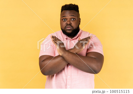 No way, absolutely not. Portrait of amazed man wearing pink shirt showing x sign with crossed hands, meaning stop, this is the end. Indoor studio shot isolated on yellow background. 100515115